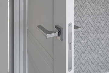 Modern metal door handle on white wooden door in interior. Knob close-up elements. Door handle, fittings for interior design