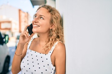 Young beautiful caucasian woman with blond hair smiling happy outdoors speaking on the phone