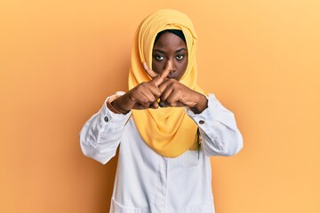 Beautiful african young woman wearing doctor uniform and hijab rejection expression crossing fingers doing negative sign