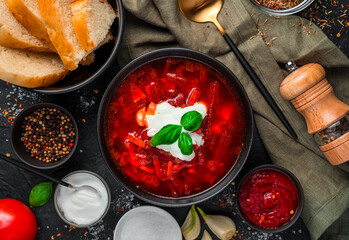 Borscht with sour cream, bread and spices on a black background.