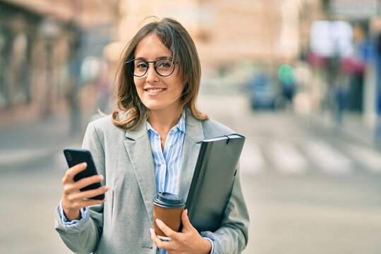 Young hispanic businesswoman using smartphone and drinking take away coffee at the city.