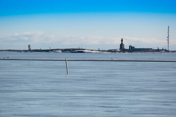 A seascape with navigation buoy sticking in the frozen sea. A small island with a lighthouse in the background.