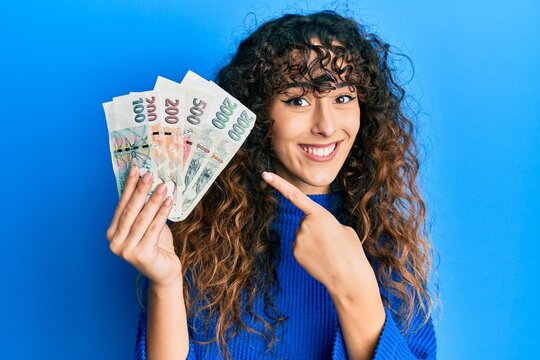 Young hispanic girl holding czech koruna banknotes smiling happy pointing with hand and finger