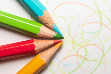 Naklejka premium Lápices de diferentes colores (azul, rojo, verde y amarillo) para colorear sobre una hoja blanca pintada y rayada con colores