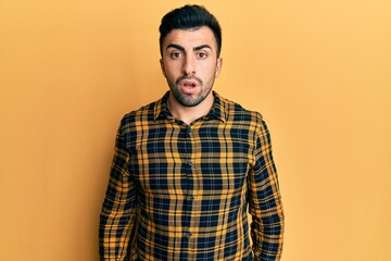 Young hispanic man wearing casual clothes in shock face, looking skeptical and sarcastic, surprised with open mouth