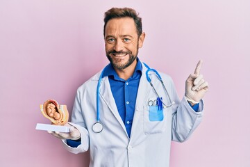 Middle age gynecologist man holding anatomical model of female uterus with fetus smiling happy pointing with hand and finger to the side