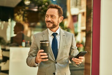 Middle age businessman using smartphone and drinking coffee at the city.