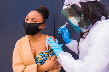Young girl receiving the injection of the coronavirus vaccine by a female doctor, antibodies,...