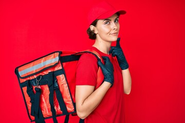 Young hispanic woman holding take away backpack serious face thinking about question with hand on chin, thoughtful about confusing idea