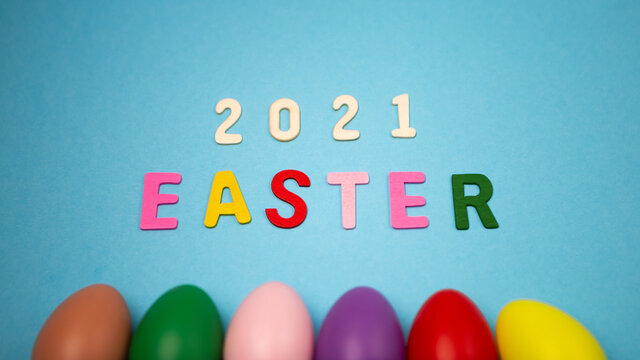Flat lay lined up set of decorated hand painted chaotically scattered colorful eggs on blue background. Happy Easter 2021 concept composition. Image with copy free space for text message

