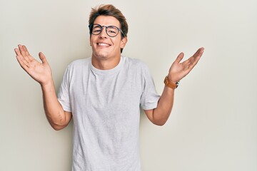 Handsome caucasian man wearing casual clothes and glasses clueless and confused with open arms, no idea and doubtful face.