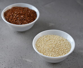Sesame and flax seed in small white plates on a gray background.