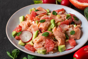 Chilean salmon seviche with grapefruit, avocado, radish, onion and mint in a plate with fork on black background. close up