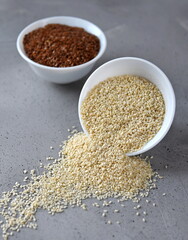 Sesame and flax seed in small white plates on a gray background.