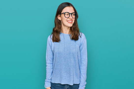 Young beautiful woman wearing casual clothes and glasses looking away to side with smile on face, natural expression. laughing confident.