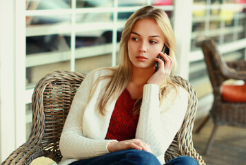 Portrait of young woman calling on a smartphone sitting at a table in cafe