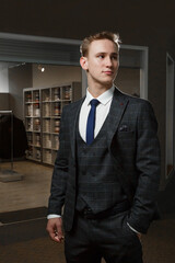 Fototapeta premium Confident elegant handsome young man standing in front of shop with clothes in handsome suit.