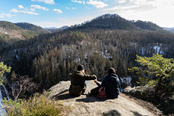 Two hikers sharing food during a break near the edge of a cliff on a big rock. Taken in the...