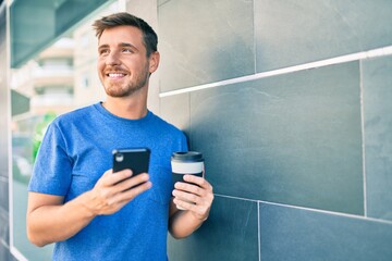 Young caucasian man using smartphone and drinking take away coffee at the city.