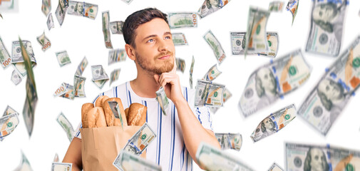 Obraz premium Handsome young man with bear holding paper bag with bread serious face thinking about question with hand on chin, thoughtful about confusing idea