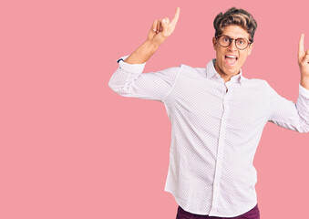 Fototapeta na wymiar Young handsome man wearing business clothes and glasses smiling amazed and surprised and pointing up with fingers and raised arms.