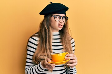 Young caucasian woman wearing french style drinking a cup of coffee skeptic and nervous, frowning upset because of problem. negative person.