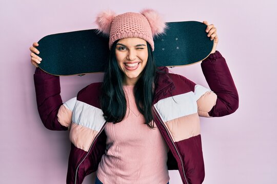 Young hispanic woman holding skate winking looking at the camera with sexy expression, cheerful and happy face.