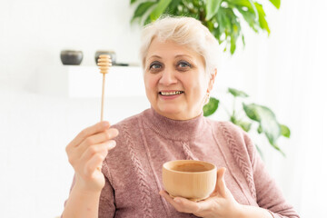 Close-up portrait of charming mature woman, holding honey jar with spoon, looking at camera, isolated on white background.