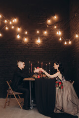 Wedding of a beautiful couple in a black dress, a bouquet of marsala color, at a festive table with candles and a cake against a black wall