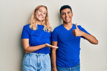 Young interracial couple wearing casual clothes showing palm hand and doing ok gesture with thumbs up, smiling happy and cheerful