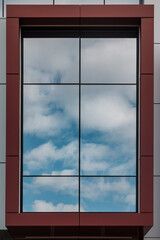 Blue sky and white clouds reflect in a window with red brown frame