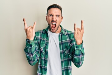 Naklejka premium Handsome man with beard wearing casual clothes shouting with crazy expression doing rock symbol with hands up. music star. heavy concept.
