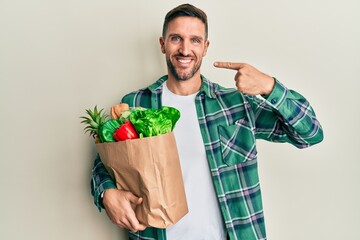 Handsome man with beard holding paper bag with groceries smiling cheerful showing and pointing with fingers teeth and mouth. dental health concept.