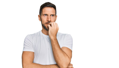 Handsome man with beard wearing casual white t shirt looking stressed and nervous with hands on mouth biting nails. anxiety problem.