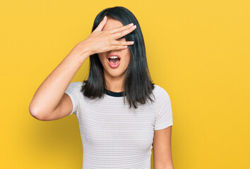 Naklejka premium Beautiful asian young woman wearing casual white t shirt peeking in shock covering face and eyes with hand, looking through fingers with embarrassed expression.
