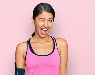 Beautiful asian young sport woman wearing sportswear and arm band winking looking at the camera...