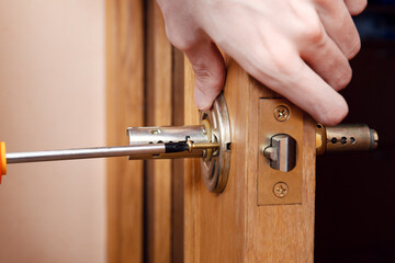 Door installation, worker Installs door knob, woodworker hands close up. A man spins the door handle with a screwdriver, repairs the door handle mechanism - obrazy, fototapety, plakaty