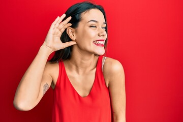 Naklejka premium Young hispanic girl wearing casual style with sleeveless shirt smiling with hand over ear listening an hearing to rumor or gossip. deafness concept.