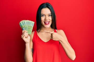 Young hispanic girl holding 1000 chilean pesos smiling happy pointing with hand and finger