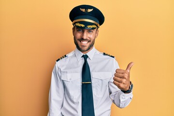 Handsome hispanic man wearing airplane pilot uniform success sign doing positive gesture with hand, thumbs up smiling and happy. cheerful expression and winner gesture. © Krakenimages.com