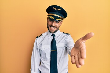 Handsome hispanic man wearing airplane pilot uniform smiling cheerful offering palm hand giving assistance and acceptance. © Krakenimages.com