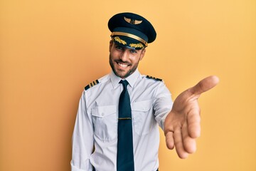 Handsome hispanic man wearing airplane pilot uniform smiling cheerful offering palm hand giving...