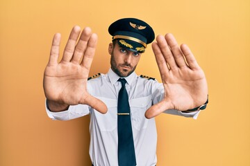 Handsome hispanic man wearing airplane pilot uniform doing frame using hands palms and fingers, camera perspective