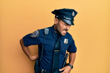 Handsome hispanic man wearing police uniform suffering of backache, touching back with hand,...
