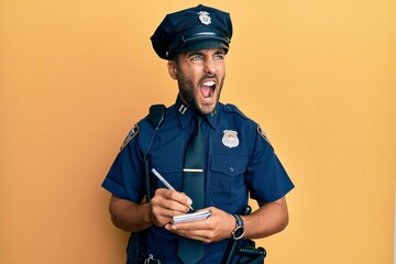 Handsome hispanic man wearing police uniform writing traffic fine angry and mad screaming...