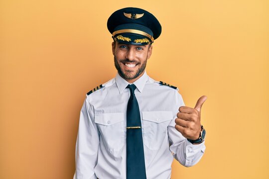 Handsome hispanic man wearing airplane pilot uniform success sign doing positive gesture with hand, thumbs up smiling and happy. cheerful expression and winner gesture.