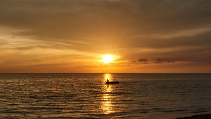 Naklejka na ściany i meble Cuba. Trinidad. Sunset in Ancon. A fisherman on a boat crosses the Sunny path