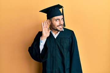 Young hispanic man wearing graduation cap and ceremony robe smiling with hand over ear listening an hearing to rumor or gossip. deafness concept.