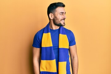 Young hispanic man football hooligan cheering game looking to side, relax profile pose with natural face and confident smile.