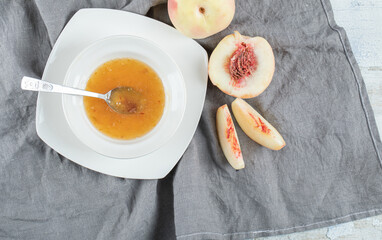 A white plate with jam and peaches on a gray tablecloth